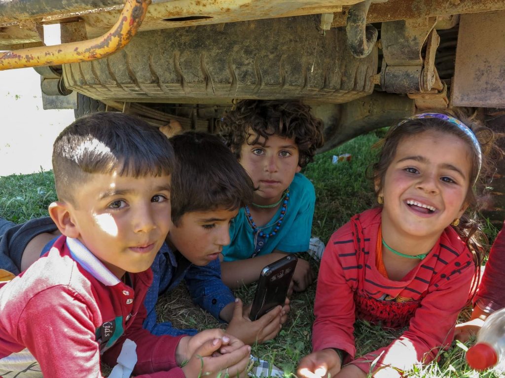 This is a photo of four young Kurdish children playing under a truck.