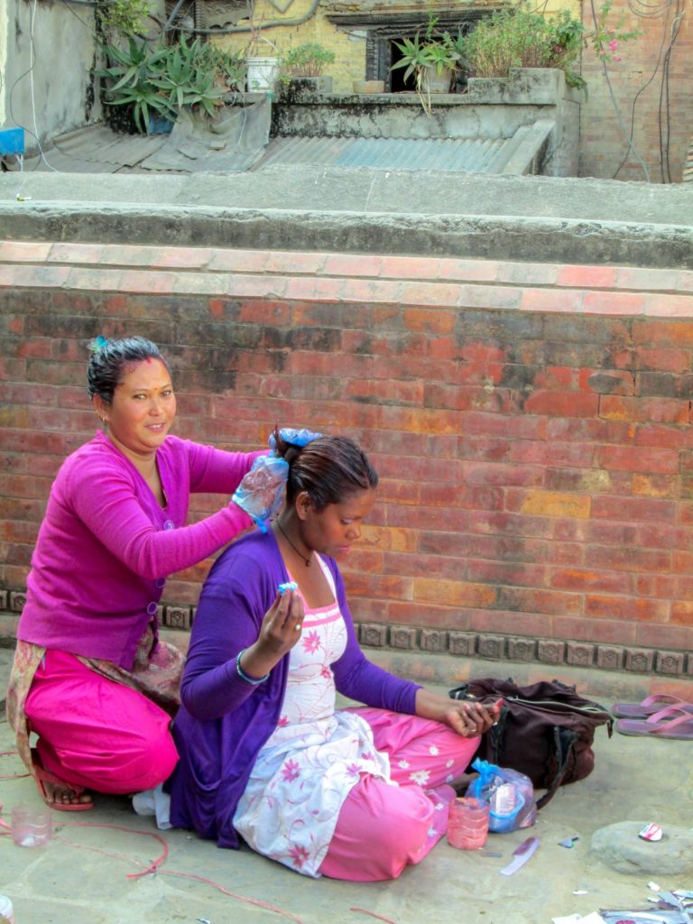This is a photo of a women dyeing a customer's hair in on the sidewalk.