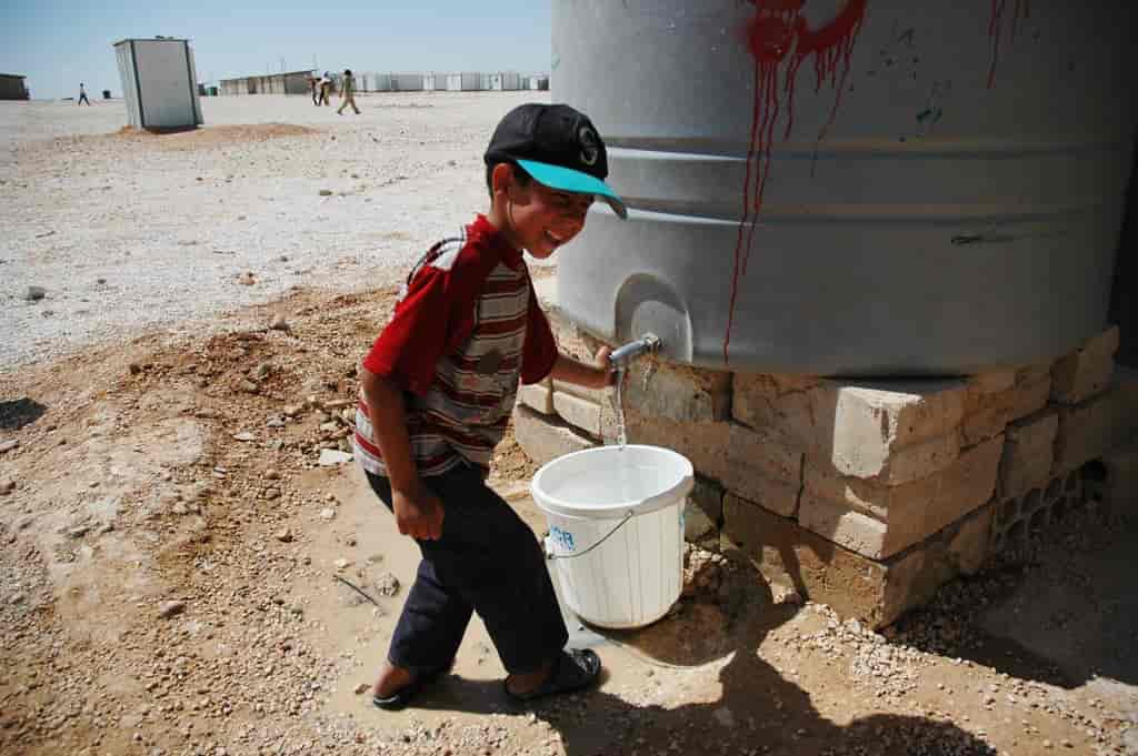 A Syrian refugee child fills a bucket of water 